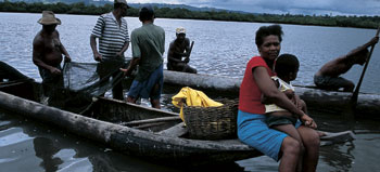 a woman and her child sit on the front of a dugout fishing boat with fishermen in the background