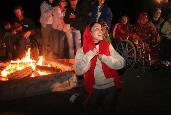 a young women, wearing a red scarf, joyously dances in front of a bonfire.