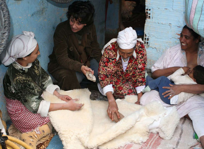 Women sit and chat as they comb out sheep skins
