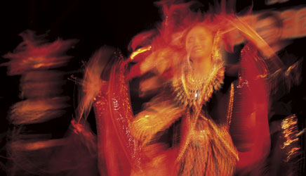 a Thai dancer shimmers in red and gold as she moves to the music