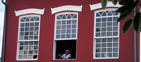 A woman looks out of the window of a red house with white windows.